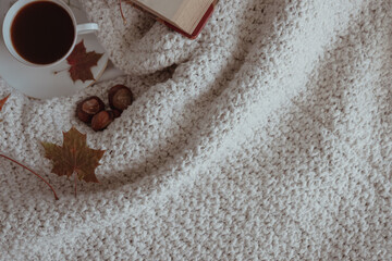 Cup of coffee, autumn maple leaves and a book on knitted texture background