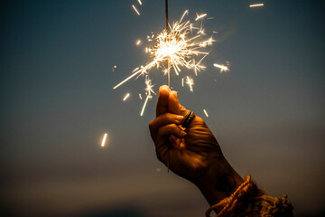 Hand holding sparkler firework firing with sunset sky in background - concept of new year eve...