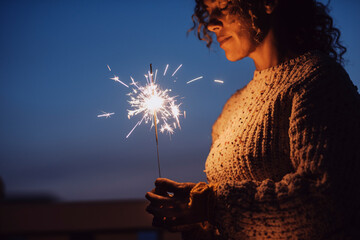 Adult woman with closed eyes holding sparkler in the night with blue sky in background - new year...
