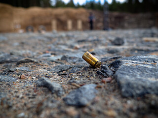 A golden 9mm bullet casing on the black ground of a shooting range after a session of gunfire
