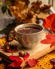 Cozy autumn morning with a cup of tea on the windowsill. Autumn still life with a cup of tea, a book and autumn leaves on a blurred background.