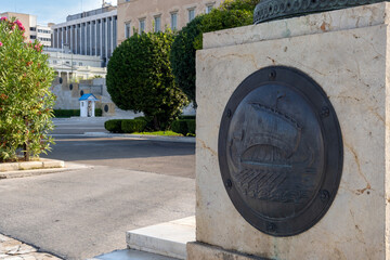 Bronze Shield representing an ancient greek ship at the entrance of the Unknown Soldier's Tomb memorial under the Greek parliament. Evzone in the background