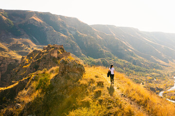 Obraz premium Female woman walks up the hill towards Tmogvi fortress surrounded by golden autumn nature and dramatic landscape in caucasus.