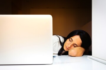Young beautiful woman sleeping face on the elbow with  laptop nearby on white desktop