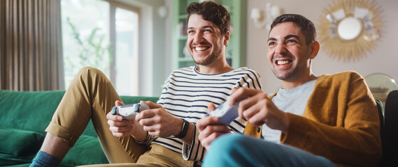 Happy Gay Couple Sitting on the Sofa Playing Video Games, Using Controllers. Competititve LGBT Men...