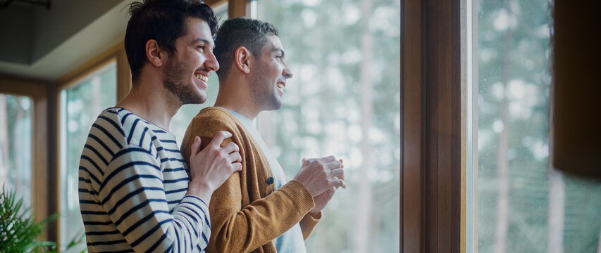 Gentle Scenes of a Stylish Young Adult Gay Couple Spend Time at Home. Two Happy Man in Love Stand in Next to a Window in Casual Clothes and Hug Each Other. Cute LGBT Relationship Content.