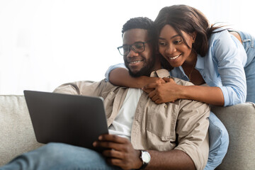 African american couple sitting on sofa, using digital tablet