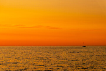 Naklejka na ściany i meble Orange and yellow sunset on the sea with a sailboat. Minimalistic photo of a silhouette of sailing boat on the sea during dusk.