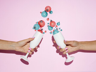 White champagne glasses toast with splashing out ornaments on a pastel pink background. Creative...