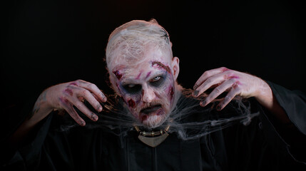 Sinister man with horrible scary Halloween zombie makeup in costume making faces, looking ominous...