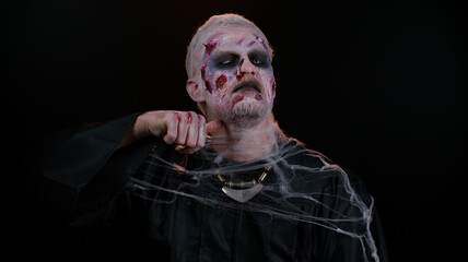 Sinister man Halloween crazy zombie with bloody wounded scars face trying to scare showing killing...
