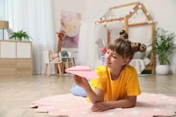 Cute little girl playing with paper plane on floor in room. Space for text