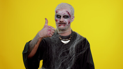 Sinister man with scary Halloween zombie makeup in costume raises thumbs up agrees with something...