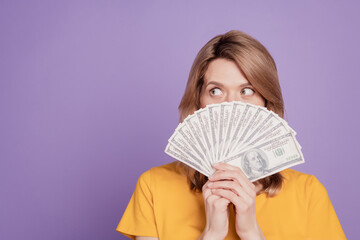 Photo of young attractive woman closing face dollars banknotes cash look empty space isolated over violet color background