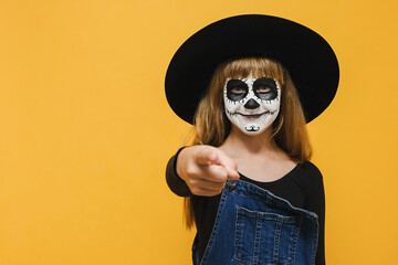 Portrait of little girl child with Halloween makeup mask wears black hat, point index finger camera on you motivation encourage, posing over yellow color background in studio. Party holiday concept