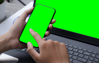 mobile phone laptop with blank green screen on desk.