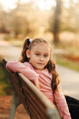 Little pretty girl sits on a bench in the park in the autumn