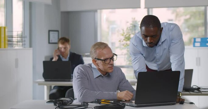 Mixed-race it-technician fix laptop for mature businessman in office