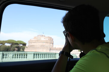 young photographer while taking a picture of the Castel Sant Angelo in Rome from inside the taxi