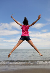 Obraz premium young girl jumping very high with open arms and legs by the sea
