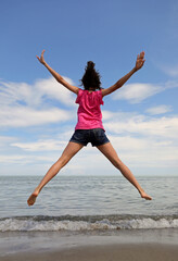 young girl jumping very high with open arms and legs by the sea