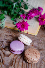 Obraz na płótnie Canvas macarons background red flowers and books, on a wooden table. Vertical frame. Aesthetics with macaroons and flowers. Beautiful cakes on a wooden table. Morning French breakfast.