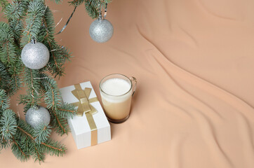 A Christmas tree, decorated with silver balls, a gift box, a glass mug with coffee and milk