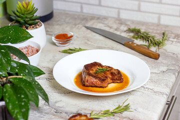 Fresh prepared roasted beef steak with spices and rosemary on white round plate on the kitchen table background.