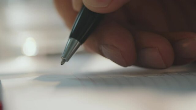 Horizontal extreme close-up shot footage of unrecognizable mans hand holding pen making marks in notebook