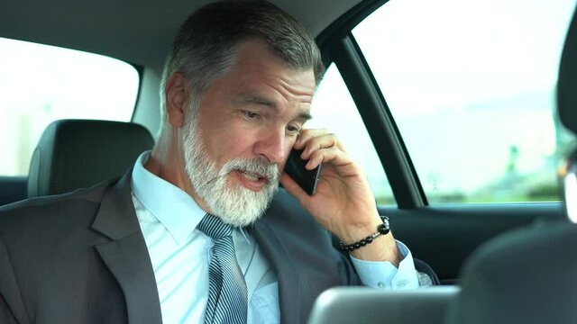 Confident Businessman talking on Phone while traveling in Business Class Car or in his Elegant Expensive Car while riding with his own Driver