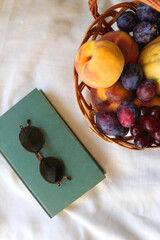 Vintage basket full of various fruit, hardback book and retro sunglasses on picnic basket. Top view.