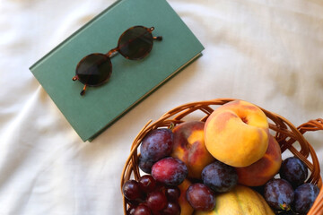 Vintage basket full of various fruit, hardback book and retro sunglasses on picnic basket. Top view.