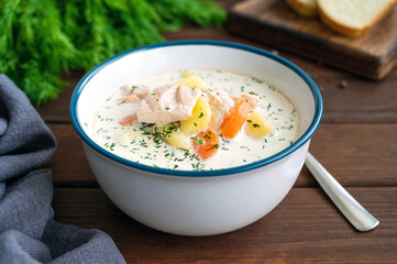 Salmon soup with cream, potatoes, carrots and herbs in a bowl on a dark wooden background. Lohikeitto soup. Copy space.