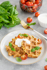 Homemade zucchini cheese waffles with sour cream and fresh basil on a plate on a gray concrete background. Vegetarian dish. Copy space.