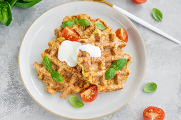 Homemade zucchini cheese waffles with sour cream and fresh basil on a plate on a gray concrete background. Vegetarian dish. Copy space.