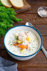 Salmon soup with cream, potatoes, carrots and herbs in a bowl on a dark wooden background. Lohikeitto soup. Copy space.