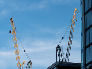 Zwei Baukräne auf einer Baustelle bei leicht bewölktem Himmel in einer Stadt.