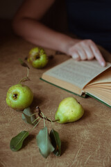 Green pears and woman reading old book at table