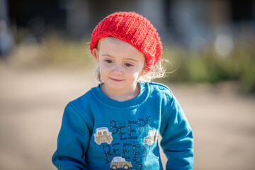 Niña con gorro de lana rojo jugando al aire libre en otoño - obrazy, fototapety, plakaty