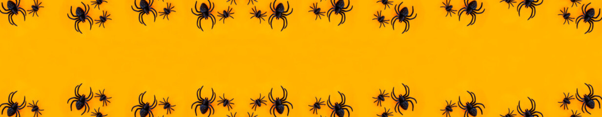Flat lay banner of black horror spiders of different sizes directed in different directions on orange backdrop with copy space. Halloween decoration spooky background concept for holidays