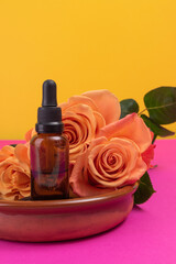 Fototapeta na wymiar glass dropper with oil extract in a bowl next to roses, natural relaxing product, product with colorful background in studio