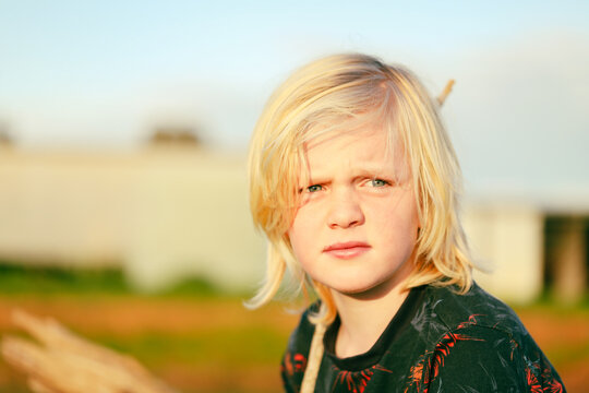 Portrait image of boy on farm holding stick with long blonde hair