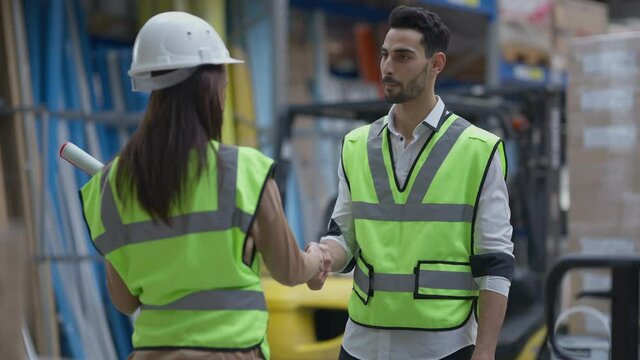 Confident Middle Eastern man passing blueprint to Caucasian woman shaking hands with colleague standing in warehouse. Portrait of professional expert manager making deal with contractor in storage