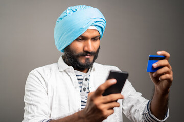 Young sikh man purchasing by paying online using credit card in mobile phone - concept of Online...