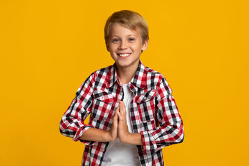 Smiling european adolescent boy modern student holds hands pressed together, prays as good mark and exam result
