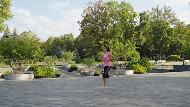 Slow motion sporty woman jogging in public park in summer. Tracking shot female jogger training in the morning. Concept of fitness