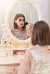 Obraz premium Beautiful young woman applying make up by mirror