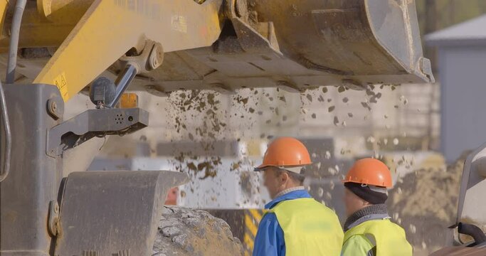 Wheel loader, with its large bucket in front, moves large amounts of gravel at the construction site. Worker and supervisor control the work on the construction site 