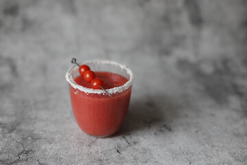 Glass of fresh red tomato juice with salt and metal stick with candy tomatoes on grey background.