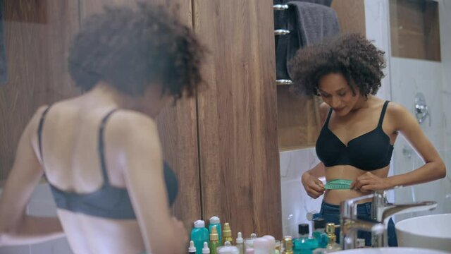 Slim black female measuring waste, happy with result, obsessed with weight loss